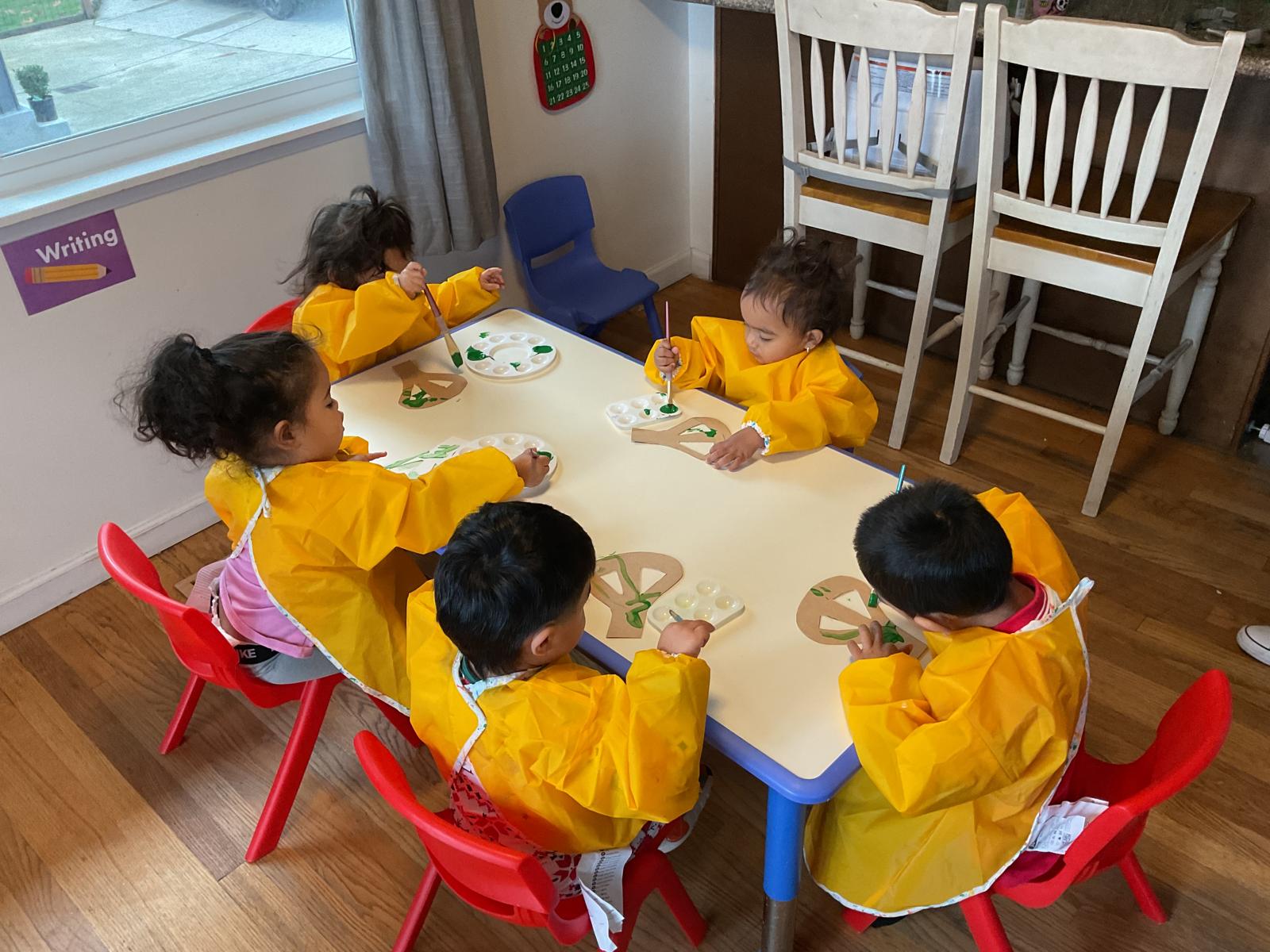 Children painting in smocks around the activity table
